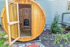A wooden sauna with a door open, revealing a bench and a heater inside.