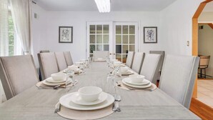 A dining room with a long table set for a meal, white walls, and framed artwork on the walls.