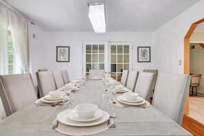 Une salle à manger avec une longue table dressée pour le repas, des murs blancs et des œuvres d’art encadrées accrochées aux murs.