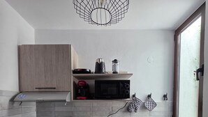 Una cocina moderna con horno integrado, microondas y un lavamanos. Hay un armario de madera sobre la encimera y una repisa con electrodomésticos.