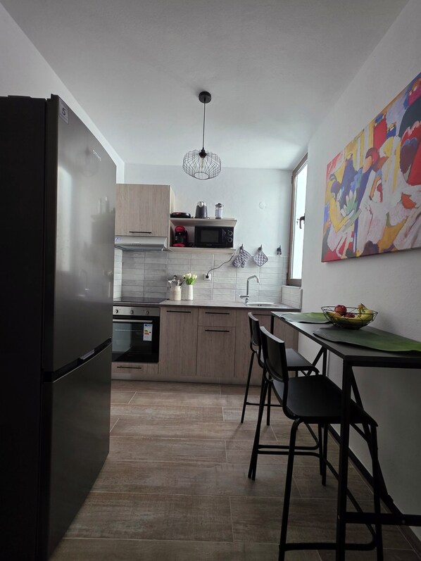 A modern kitchen with a refrigerator, microwave, and stove. There is a dining table with chairs and a colorful painting on the wall.