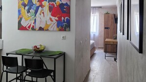 Un interior moderno con una zona de comedor que incluye una mesa y sillas, un cuadro abstracto y colorido en la pared, y un pasillo que conduce a otra habitación.
