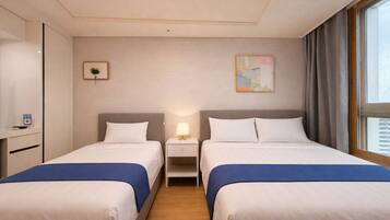A hotel room with two beds, a desk, a lamp, and a painting on the wall.