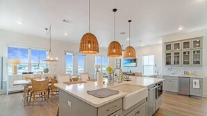 Een moderne keuken met een groot eiland, hanglampen en uitzicht op de oceaan.