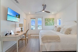 A bedroom with a bed, desk, chair, TV, ceiling fan, and a view through a door.