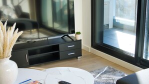 Una sala de estar moderna con un televisor de pantalla plana, una mesa de centro con revistas, un control remoto y una planta en maceta.
