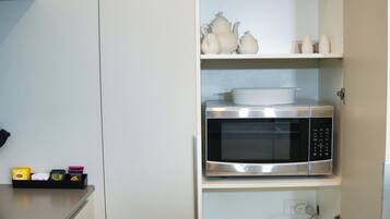 Una cocina con un microondas en el estante central, un bol de vidrio en el estante superior y algunos utensilios de cocina en los estantes inferiores.