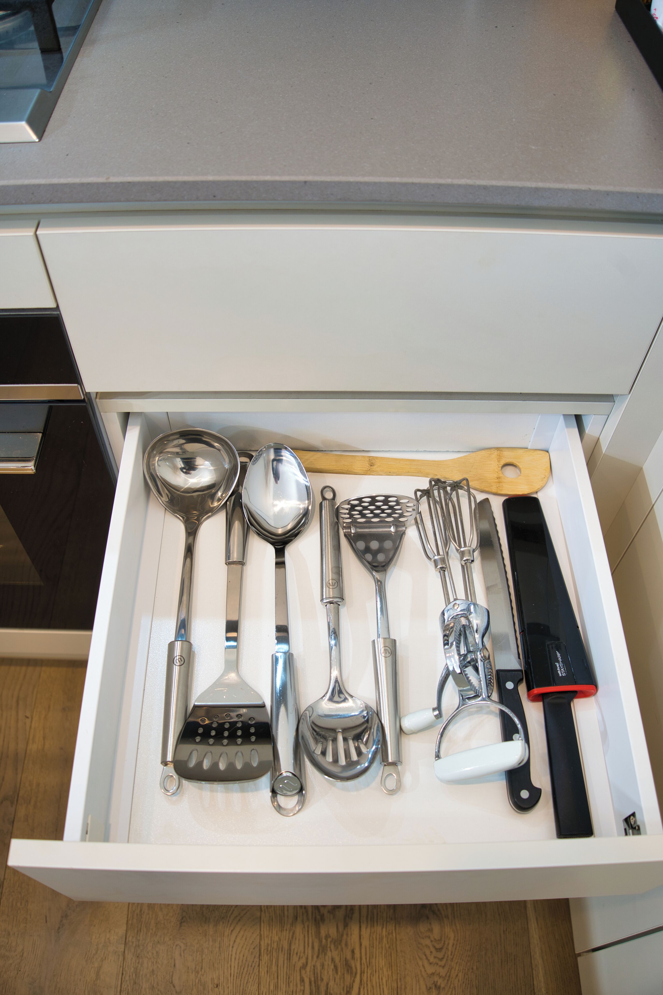 A drawer containing various kitchen utensils including a spoon, spatula, grater, and knife.