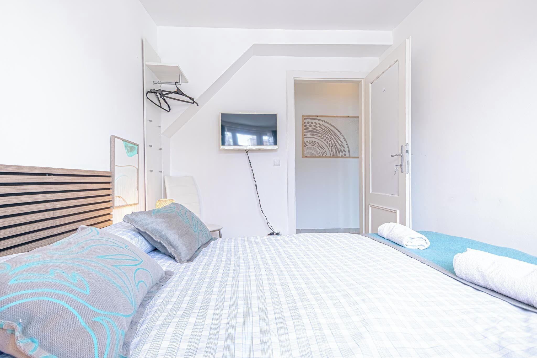 Une chambre à coucher moderne, avec un lit, un téléviseur fixé au mur et une porte donnant sur une autre pièce.