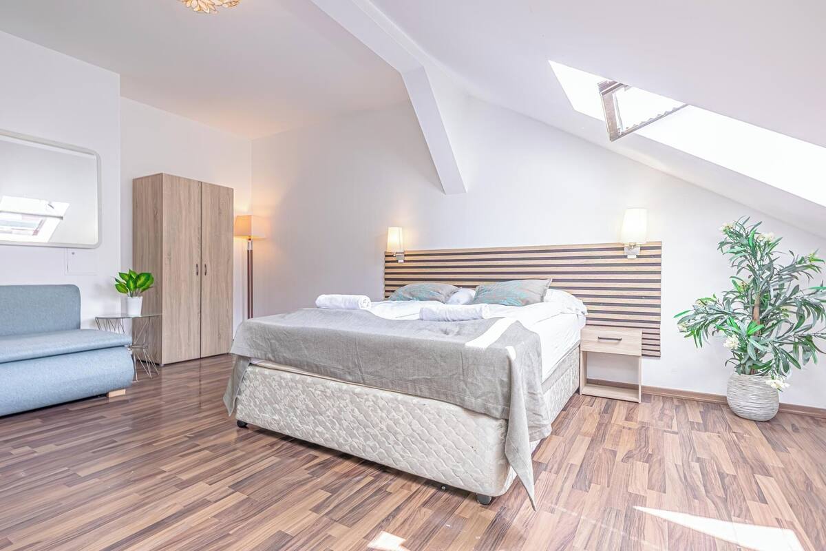 Ein modernes Schlafzimmer mit Schlafgalerie, einem Bett mit Holz Kopfteil, einem Nachttisch mit Lampe, einer kleinen Pflanze und einem blauen Sofa.