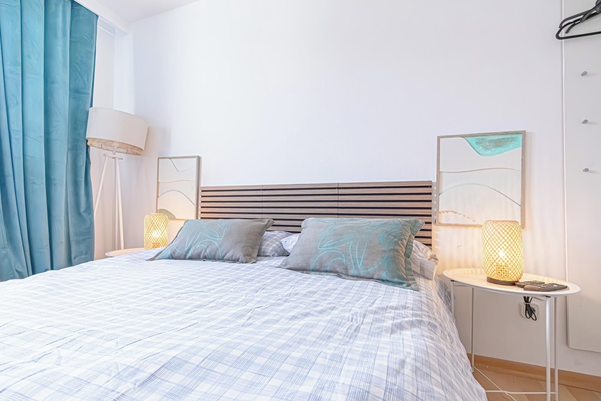 A neatly made bed with a checkered bedspread, two bedside lamps, and a bedside table with a lamp.