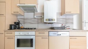 Une cuisine moderne avec des meubles de couleur bois clair, un lave-vaisselle en acier inoxydable, un four encastré, une cuisinière à gaz et une hotte aspirante.