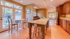 A spacious kitchen with a large island, wooden cabinets, and a view through the glass doors. - Beautiful home in the heart of Sea Pines on the 11th green of Heron Point! (Hilton Head Island)
