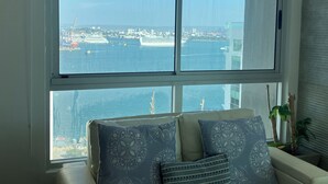 A room with a large window overlooking a harbor with ships and buildings.