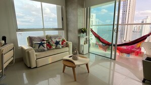 A spacious living room with a large window, a sofa, a coffee table, and a hammock.