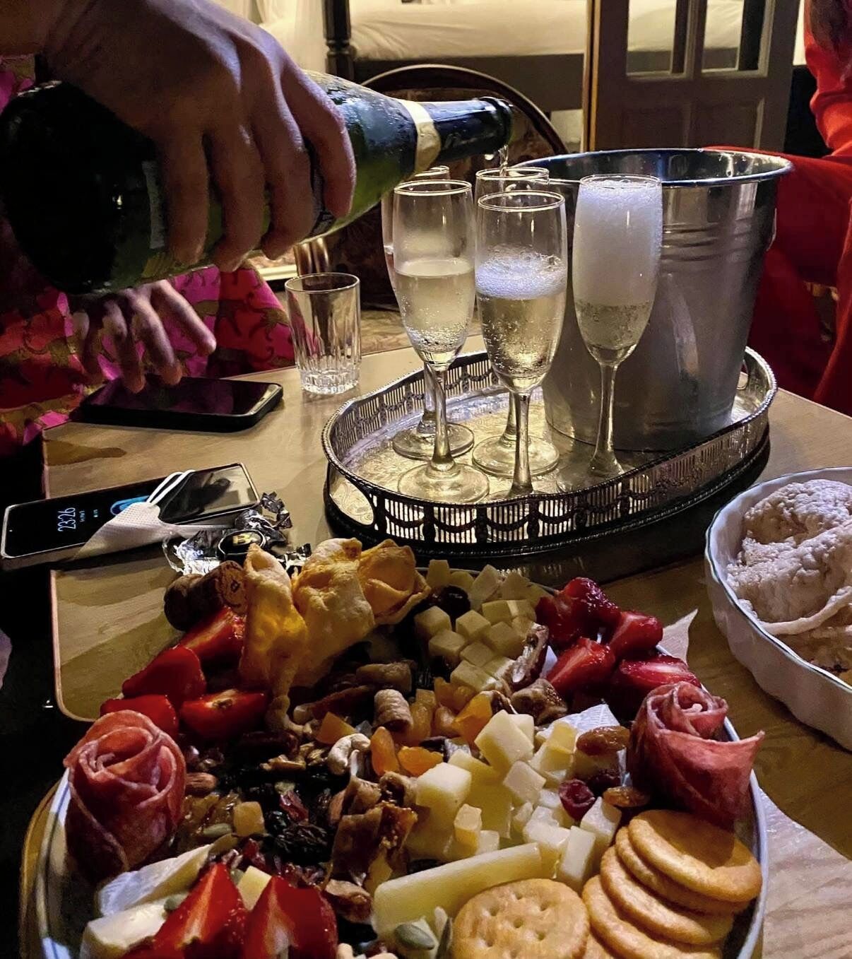 A table with a charcuterie board, glasses, and a bottle being poured.
