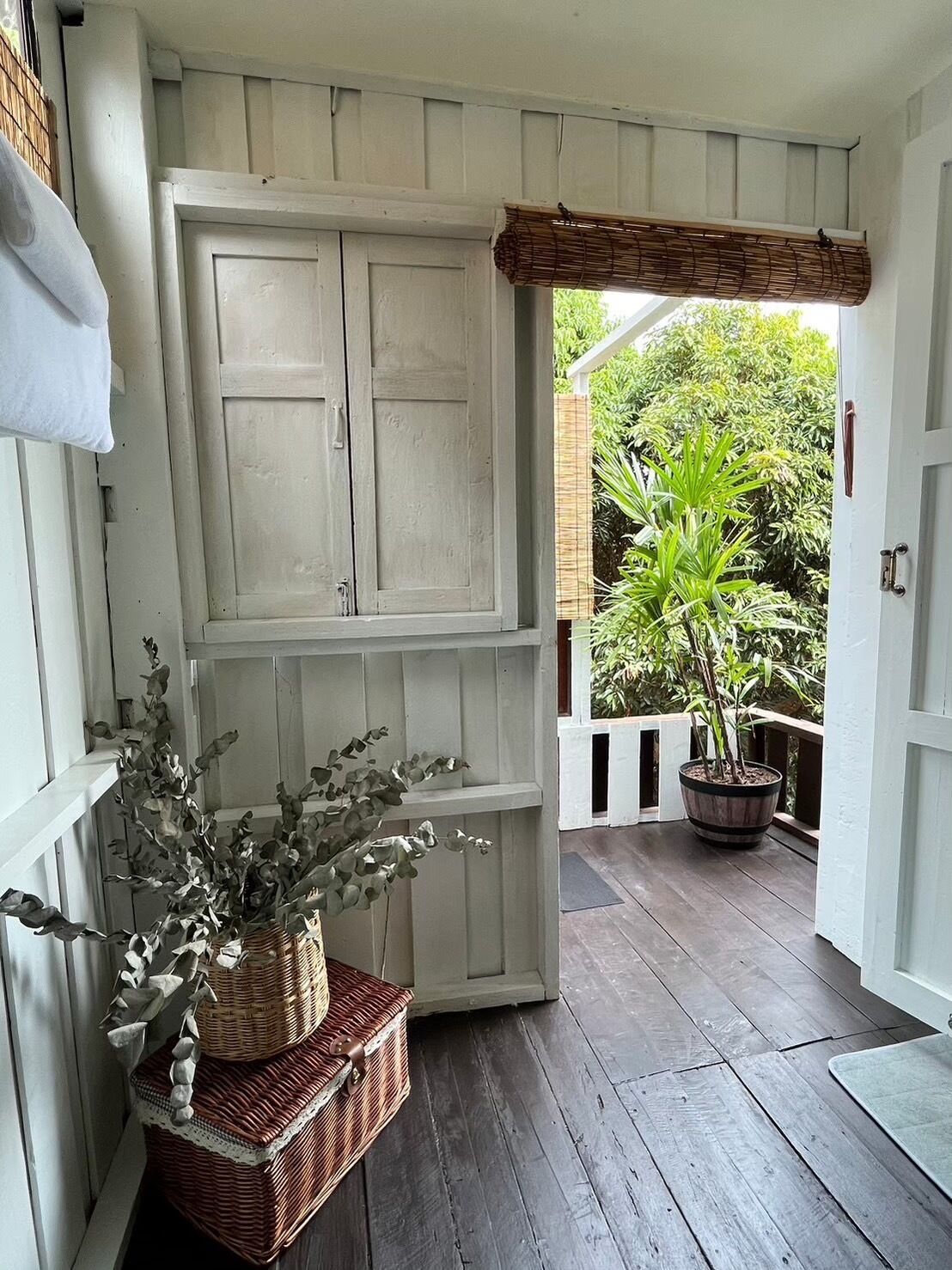 Une véranda en bois avec une porte blanche, un panier en osier et une plante en pot.