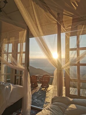 Una habitación con una cama, dos sillones de mimbre y vistas a la montaña a través de amplias ventanas.