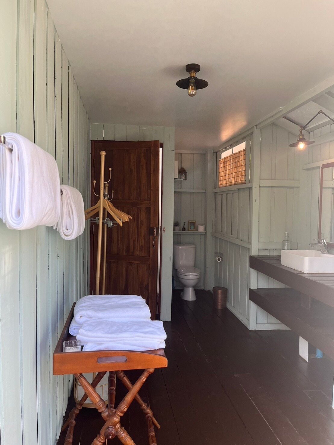 A bathroom with a wooden door, a white toilet, a sink, and a towel rack.