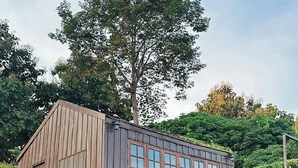 A wooden building with large windows, surrounded by lush greenery and a tree. - 4000Dao-A Hilltop Hideaway Experience  (Mae Chan)