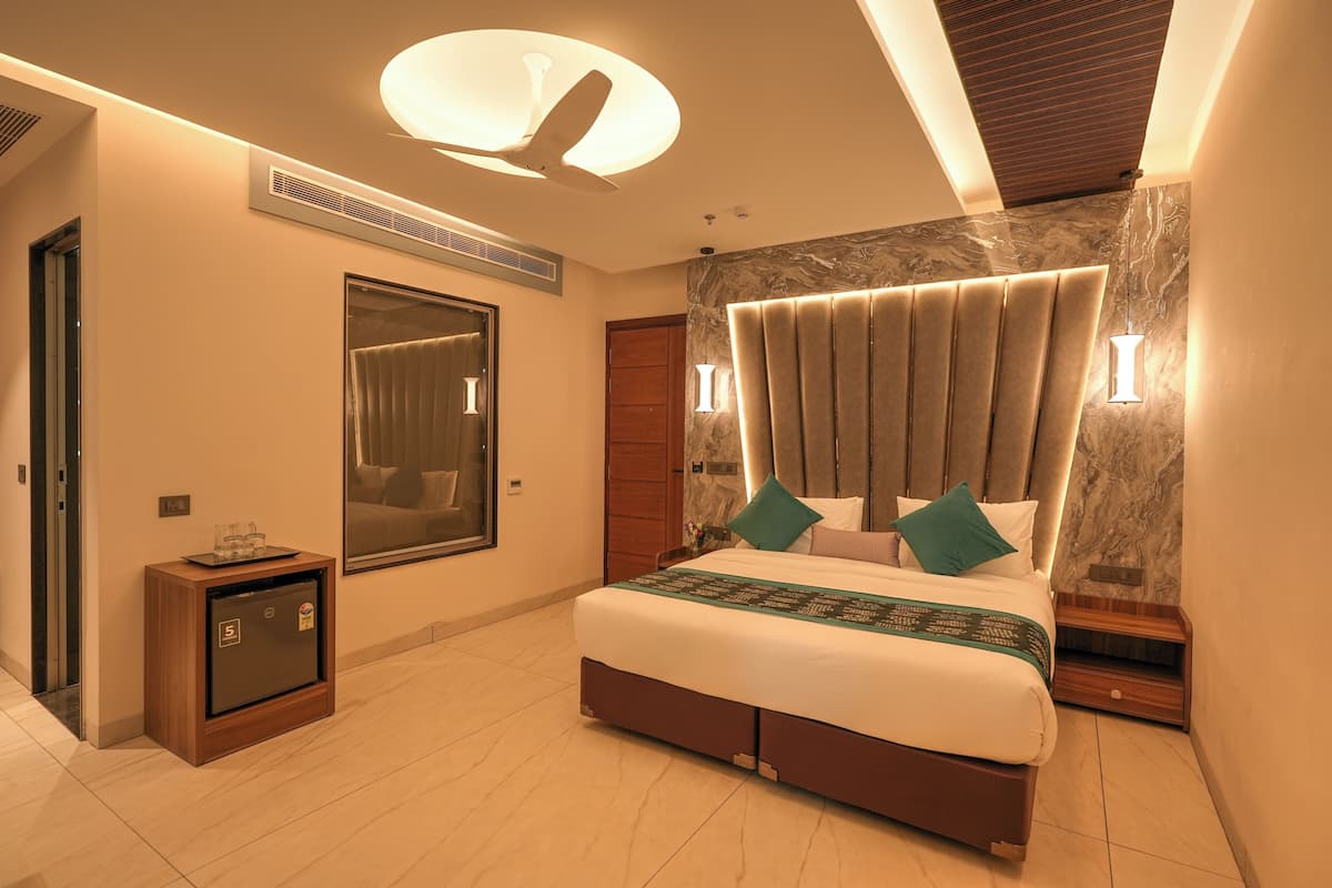 A modern hotel room with a large bed, a built-in safe, a mirror, and a ceiling fan.