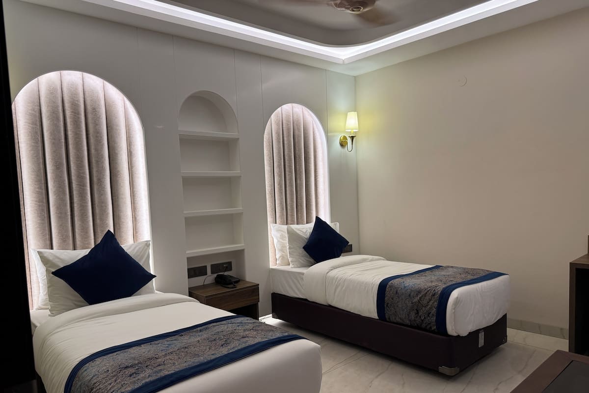 A hotel room with two beds, a nightstand, a lamp, and a ceiling light.
