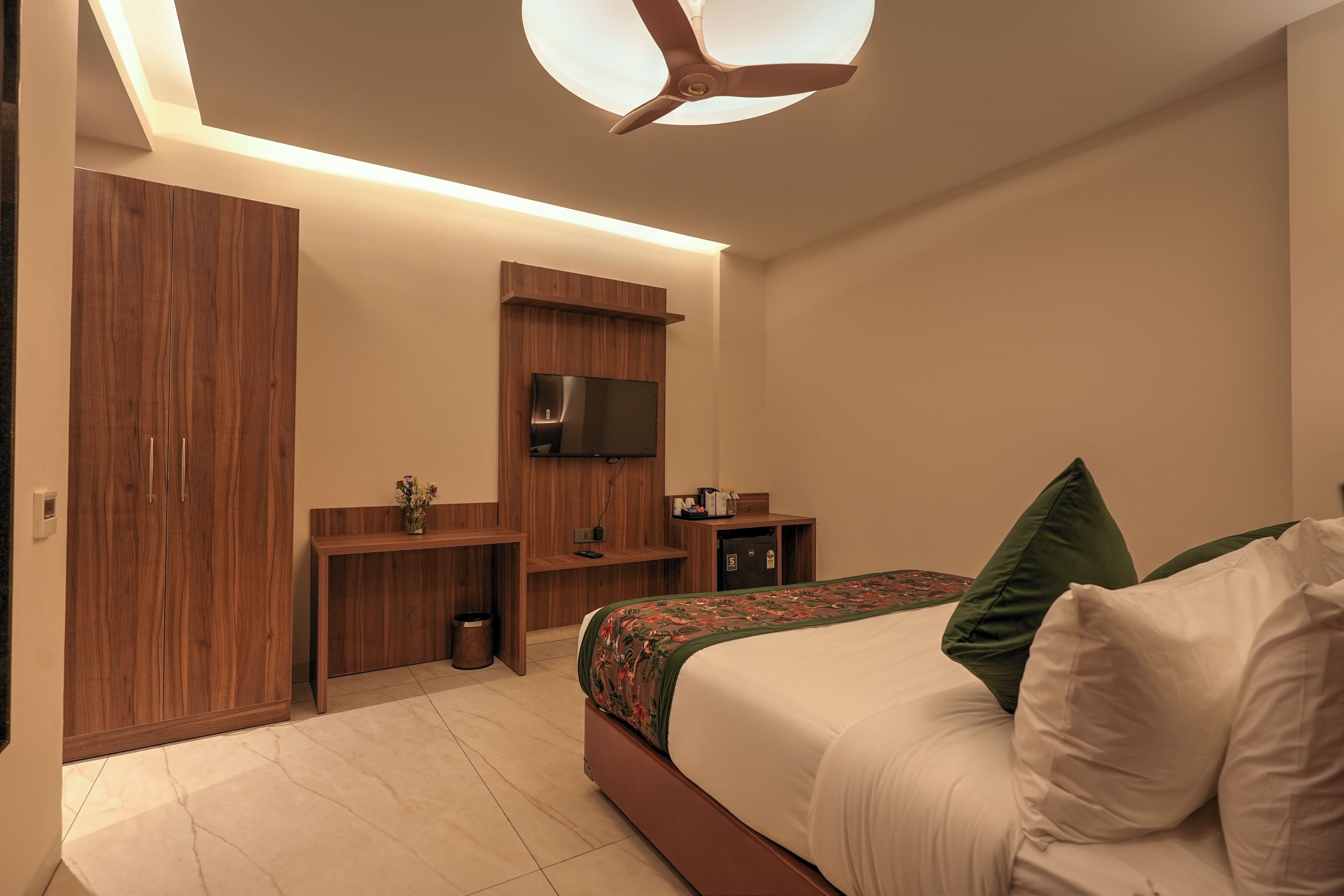 A modern bedroom with a bed, wooden wardrobe, TV, and a small desk.