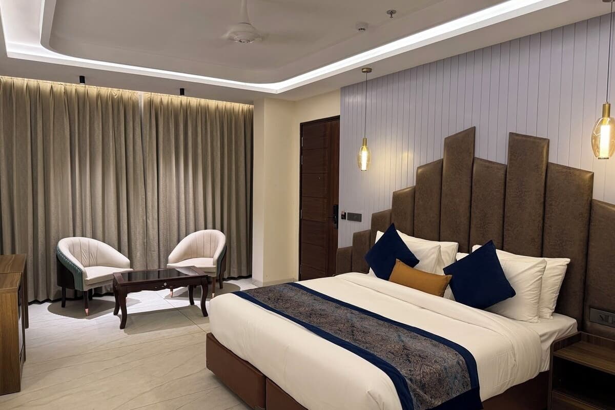 A modern hotel room with a large bed, two armchairs, a wooden coffee table, and a ceiling fan.