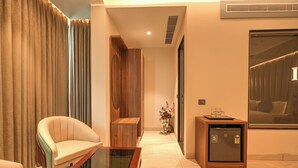 A modern living room with a glass coffee table, a sofa, a wooden cabinet, and a small refrigerator. - RC Dream Place (Greater Noida)