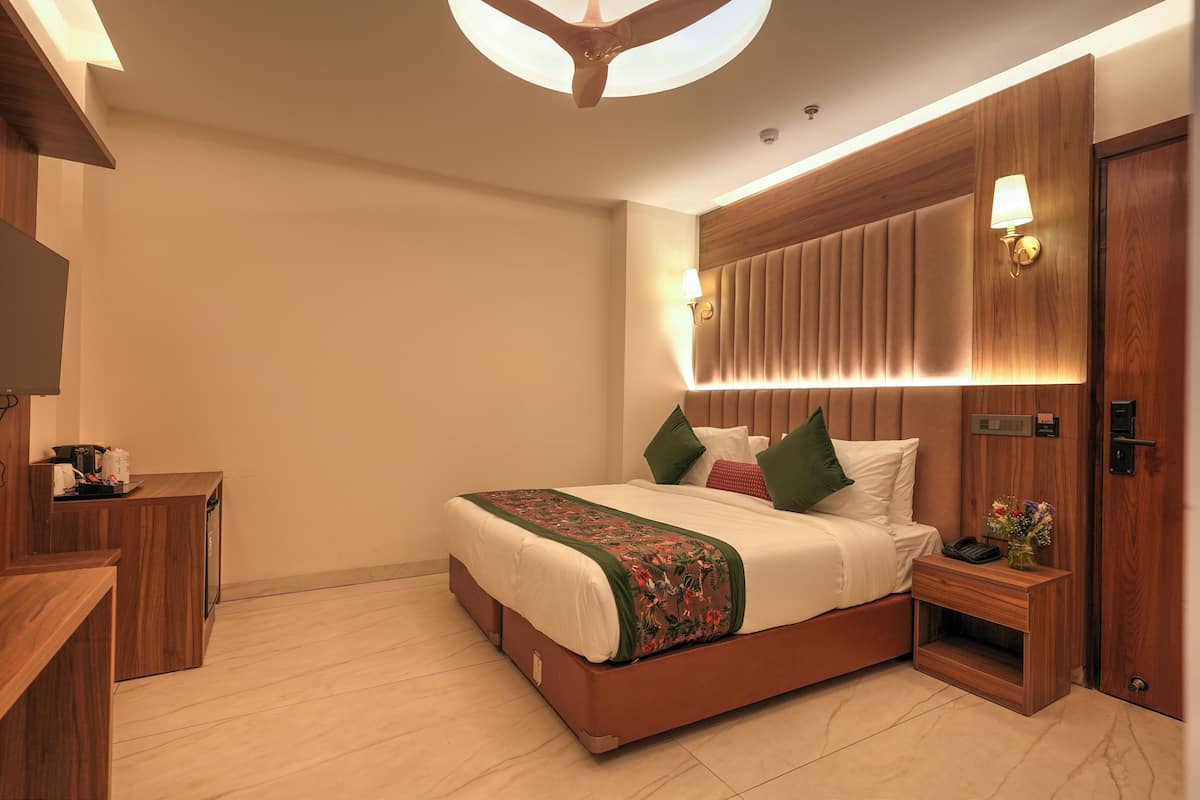 A modern hotel room with a wooden bed, bedside table, and a built-in headboard with integrated lighting.