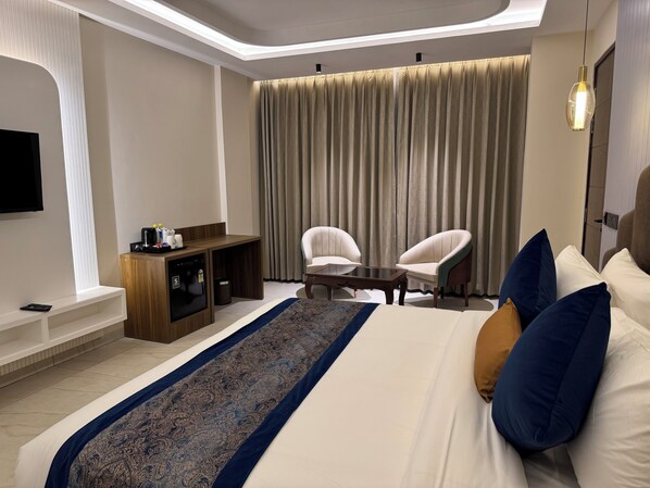 A hotel room with a bed, two chairs, a coffee machine, a TV, and a large window with curtains. - RC Dream Place (Greater Noida)
