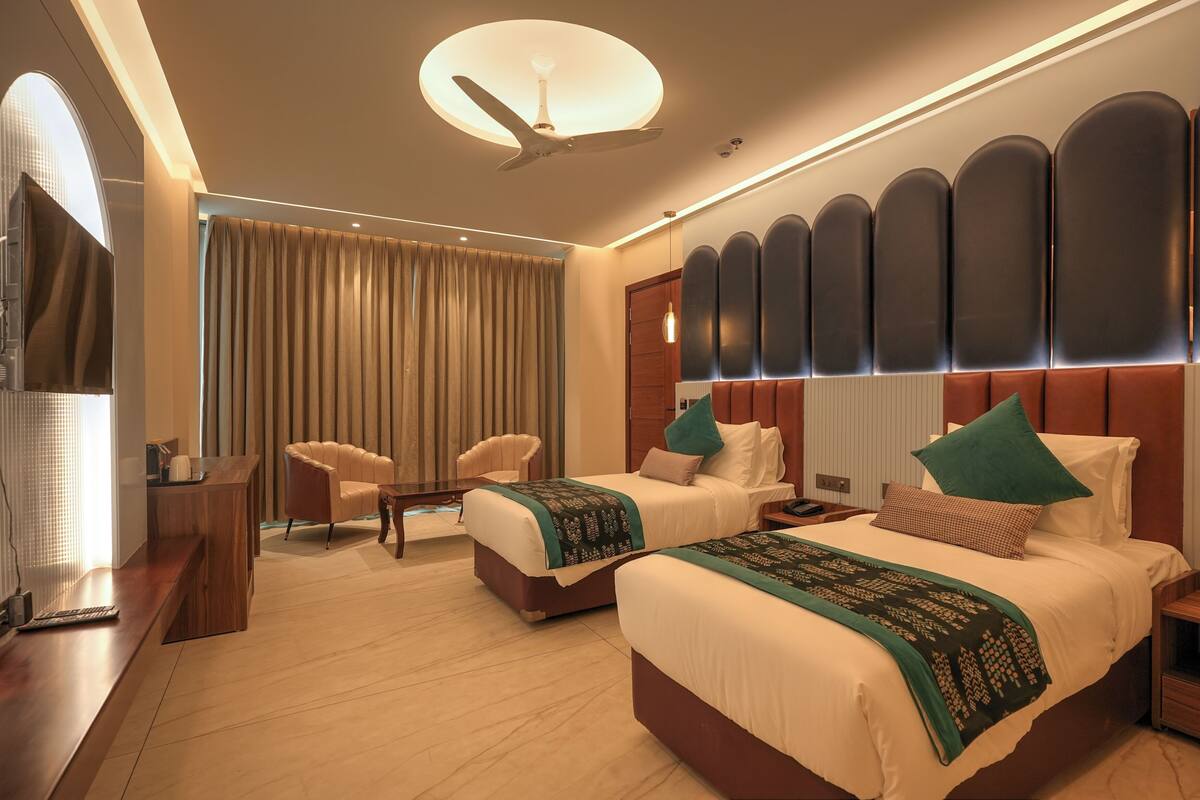A hotel room with two beds, a desk, a chair, and a large window with curtains.