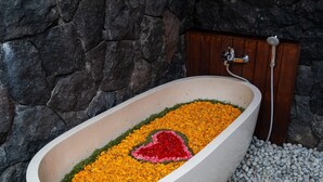 Een bad gevuld met gele bloemen en een rood hart, voor een stenen muur met een houten deur.