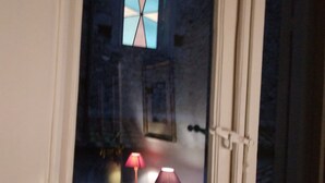 Une chambre comprenant un lit, deux lampes de chevet, une fenêtre ornée de vitraux et une porte.