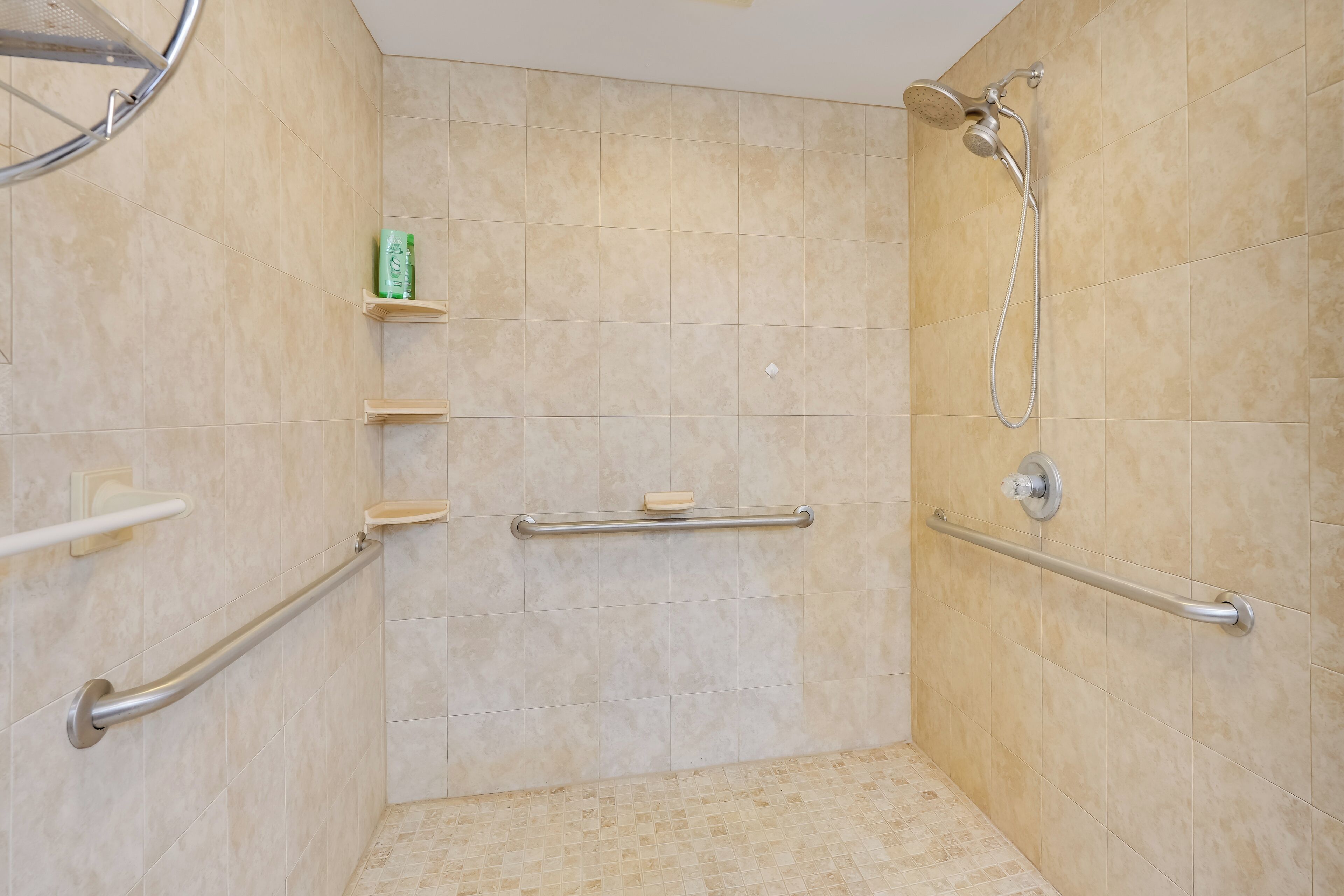 A shower area with beige tiles, a handheld showerhead, and grab bars.
