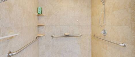 A shower area with beige tiles, a handheld showerhead, and grab bars.