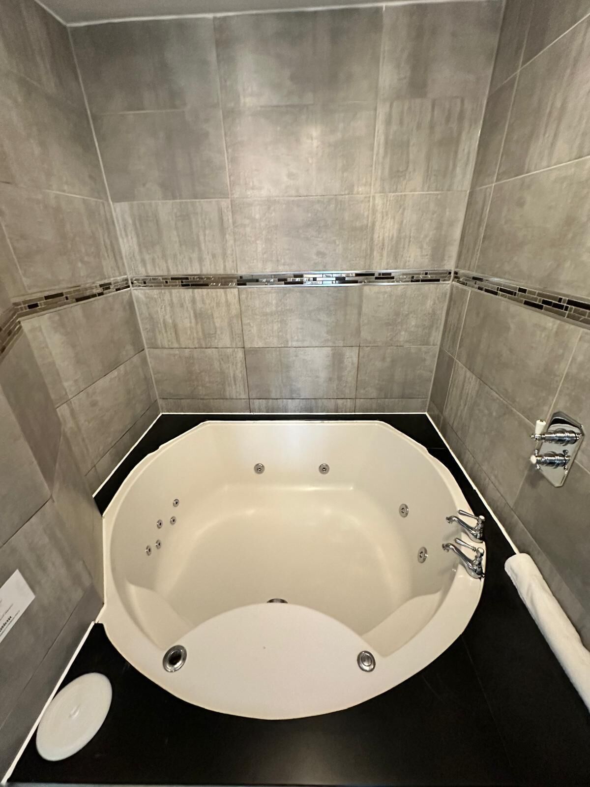 A modern bathroom with a freestanding bathtub, a black countertop, and grey tiled walls.