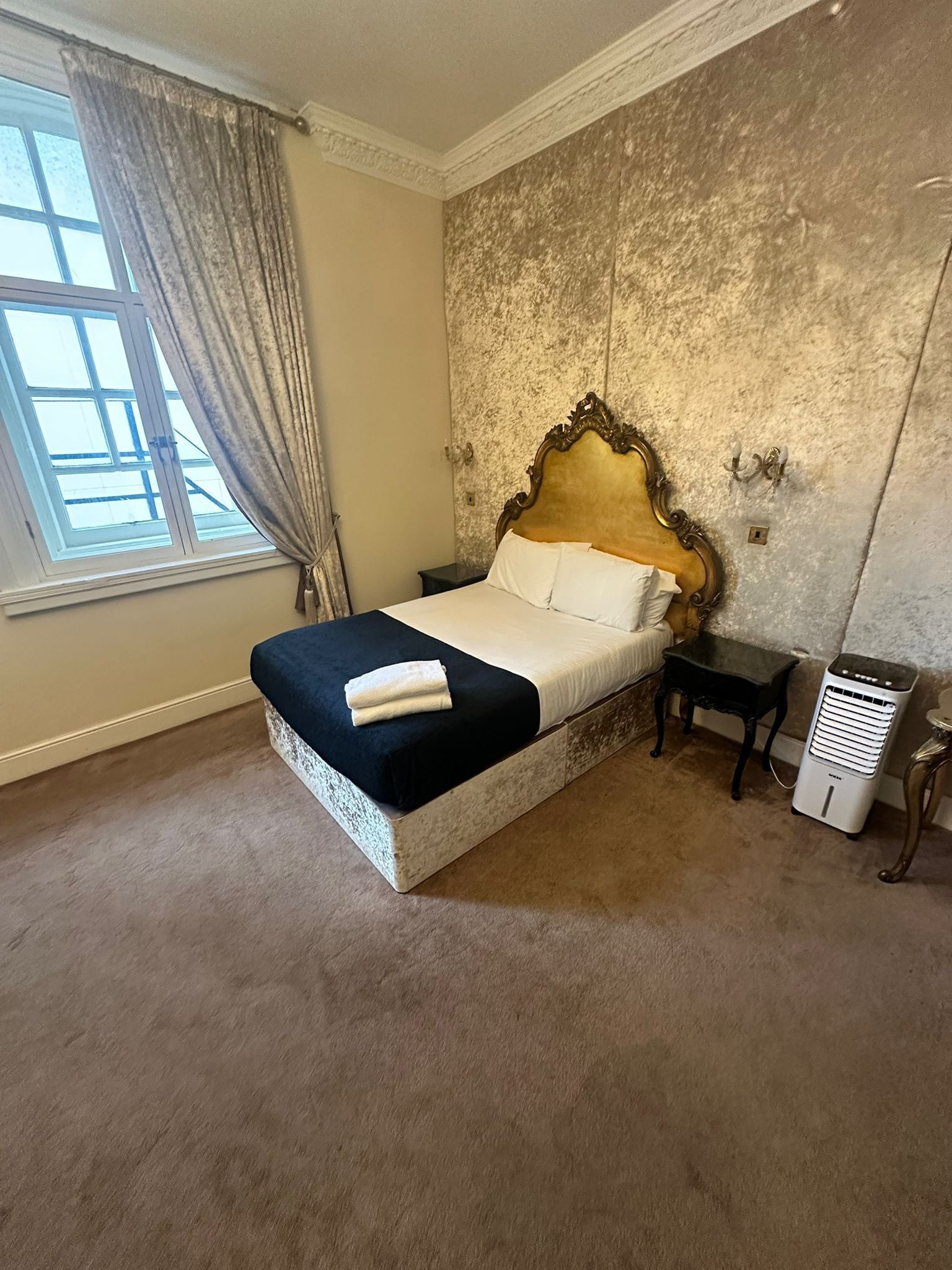 A bedroom with a large bed, a nightstand, a heater, and a window with curtains.