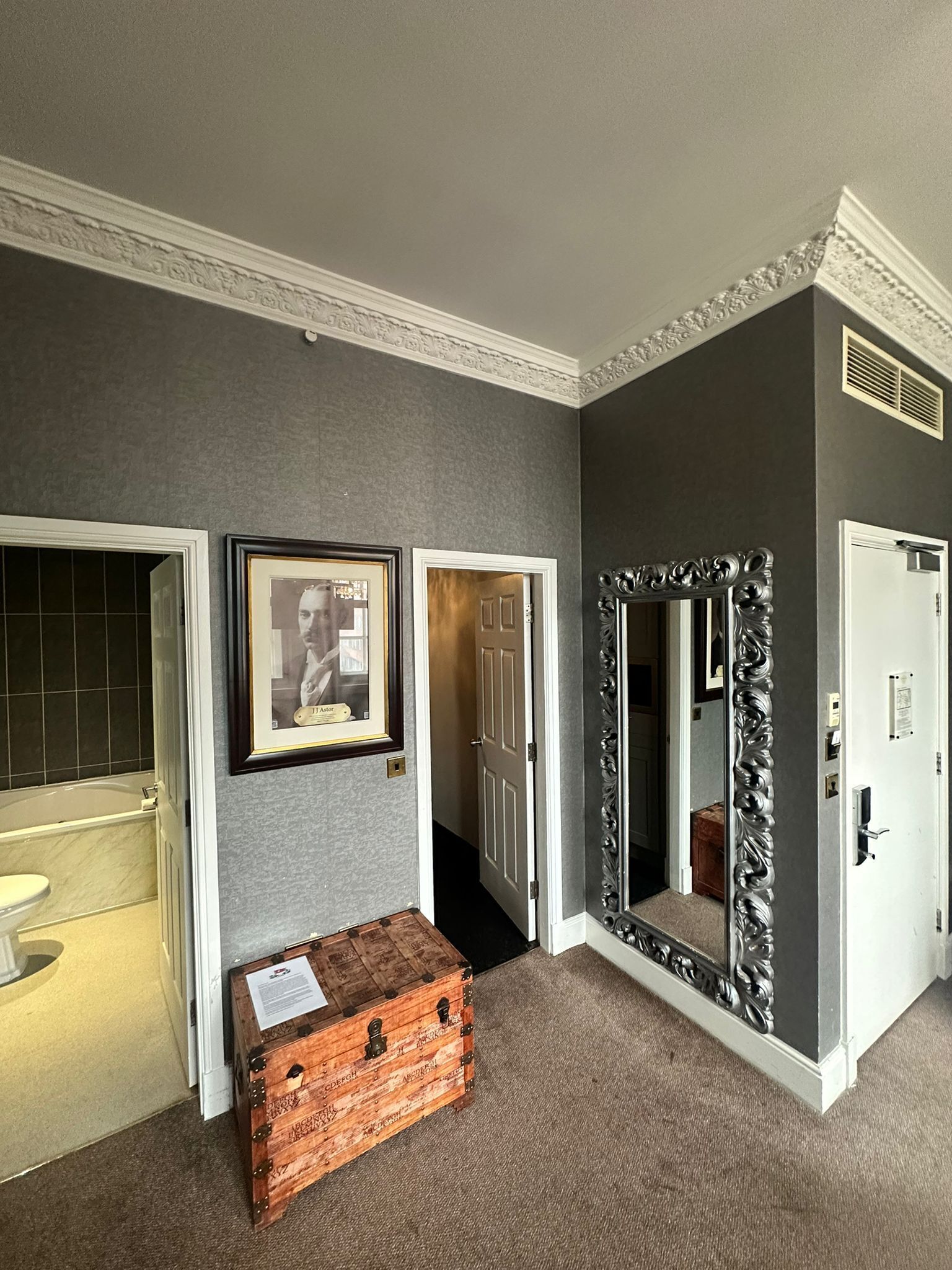 A hallway with a wooden chest, framed pictures, and a mirror with an ornate frame.