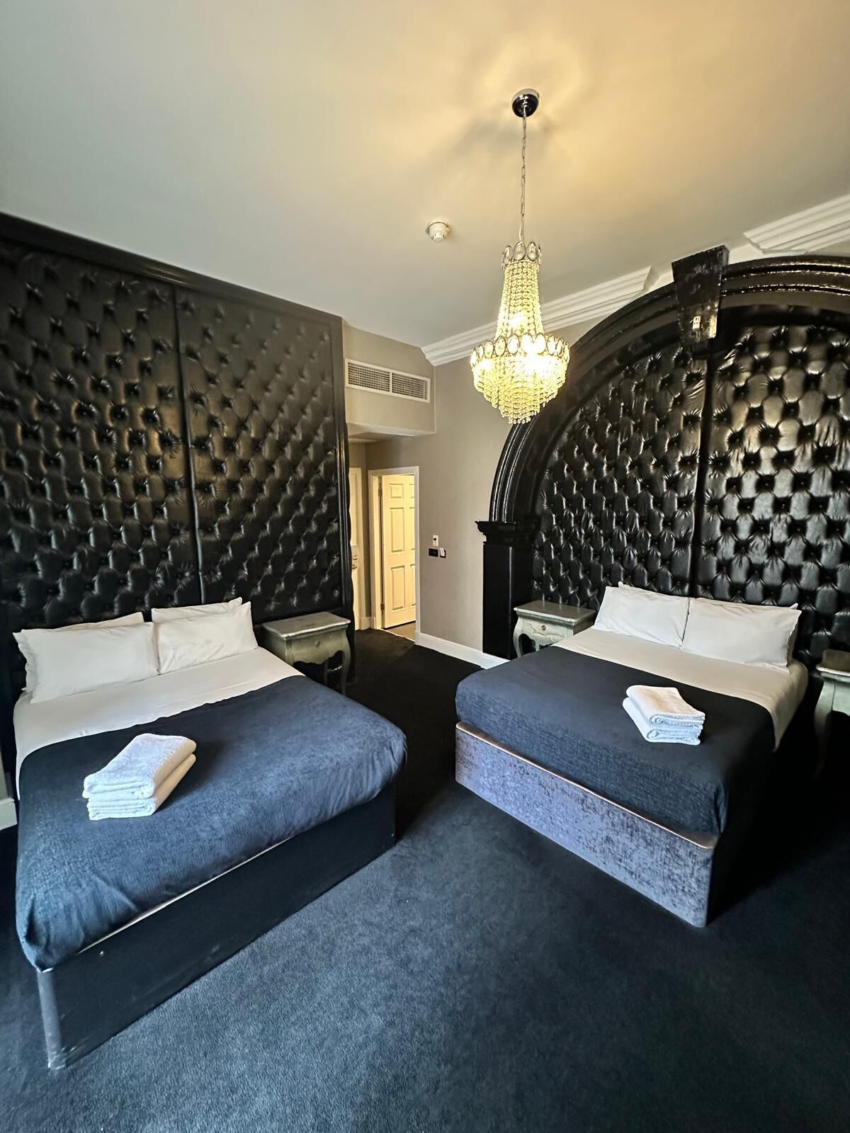 A hotel room with two beds, a chandelier, and a checkered headboard.