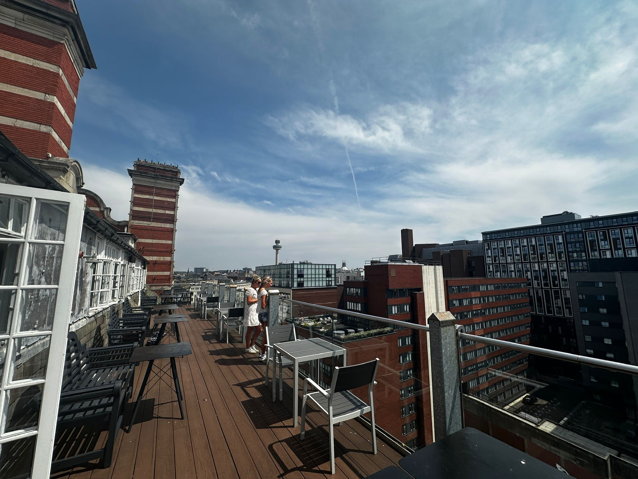 A rooftop terrace with outdoor seating, a view of the city, and a tall chimney.
