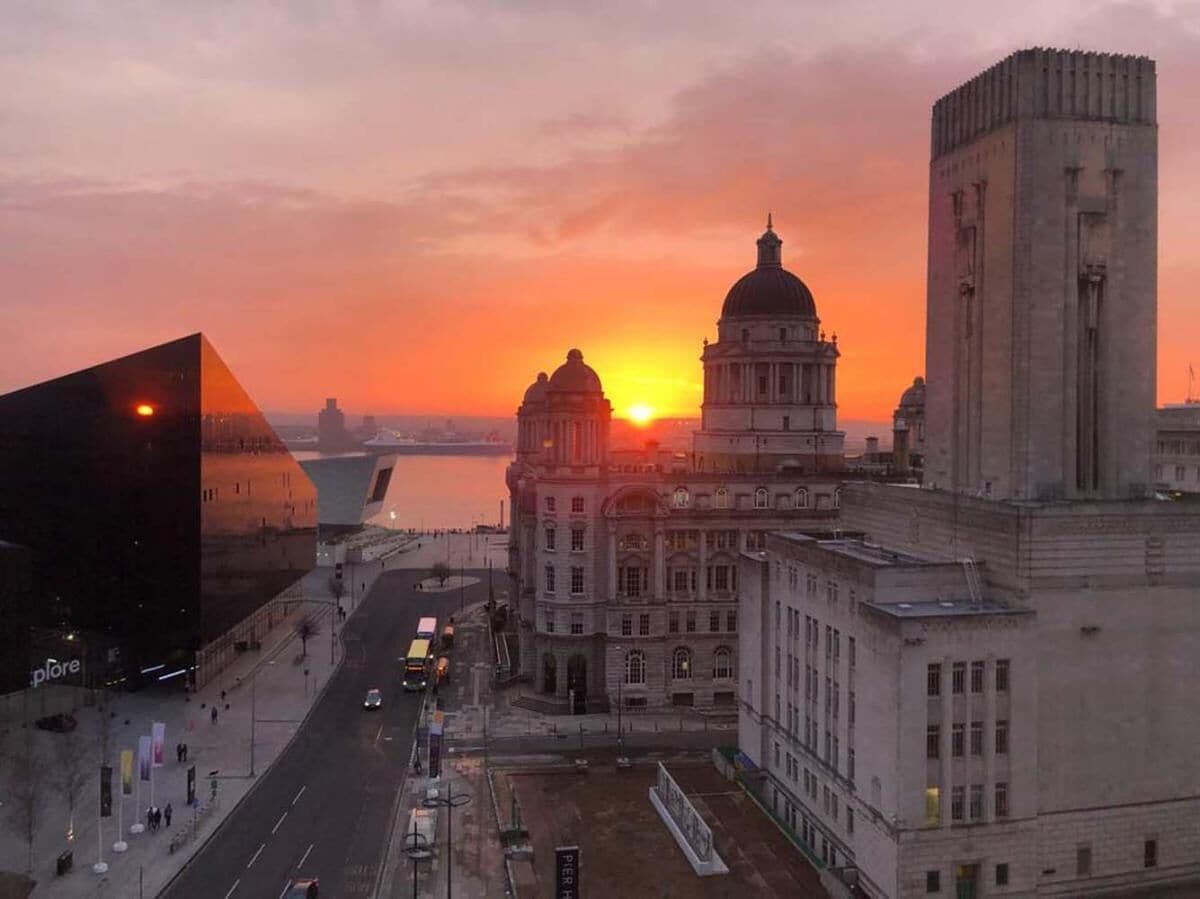 A cityscape with a prominent building featuring a dome and a tall tower, set against a sunset.