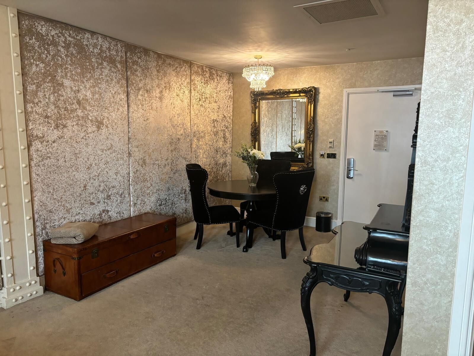 A dining area with a table, chairs, a chandelier, a mirror, and a vintage suitcase.