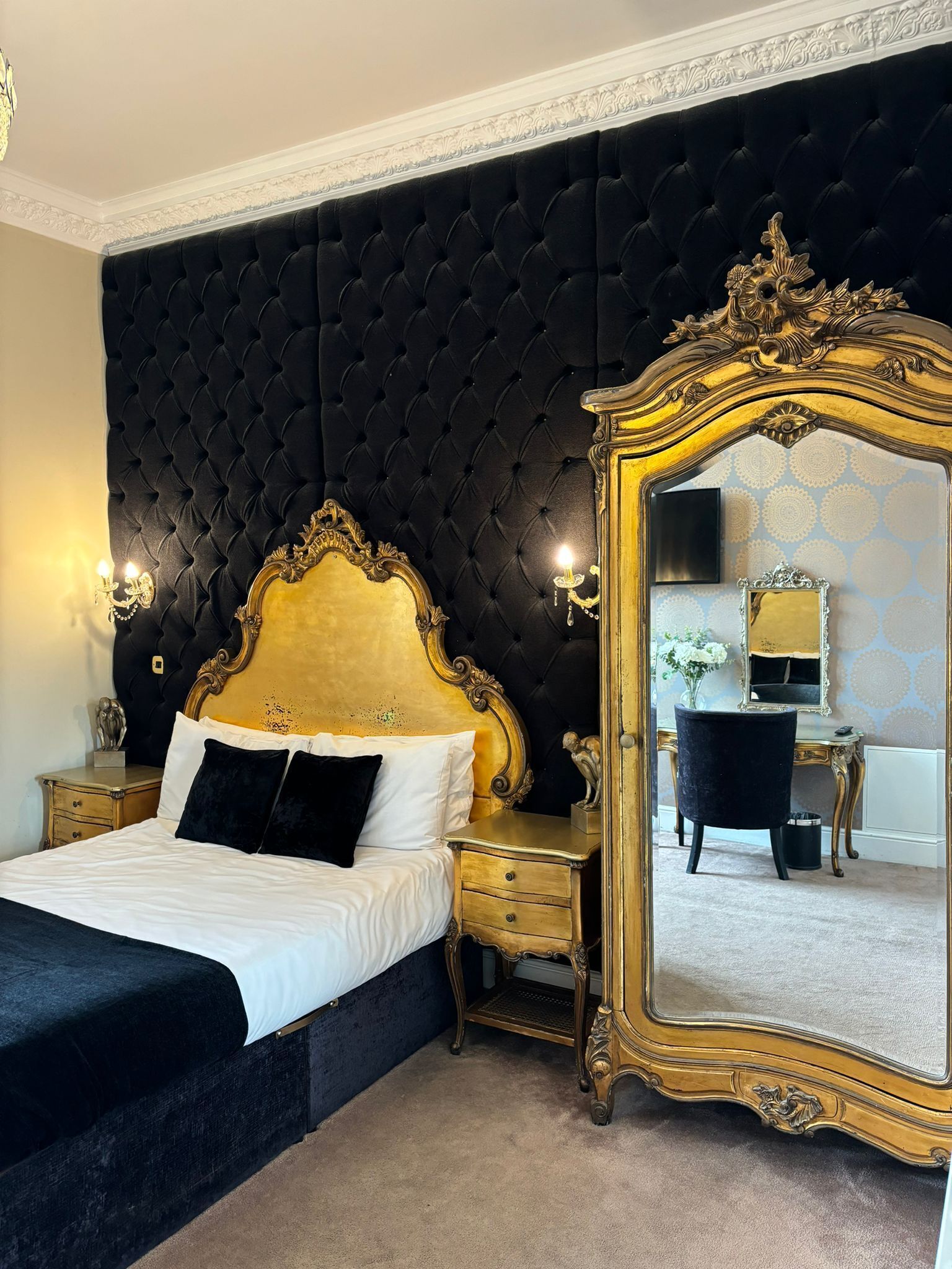 Um quarto luxuoso com cabeceira estofada, um espelho grande e decorativo e um elegante aparador.