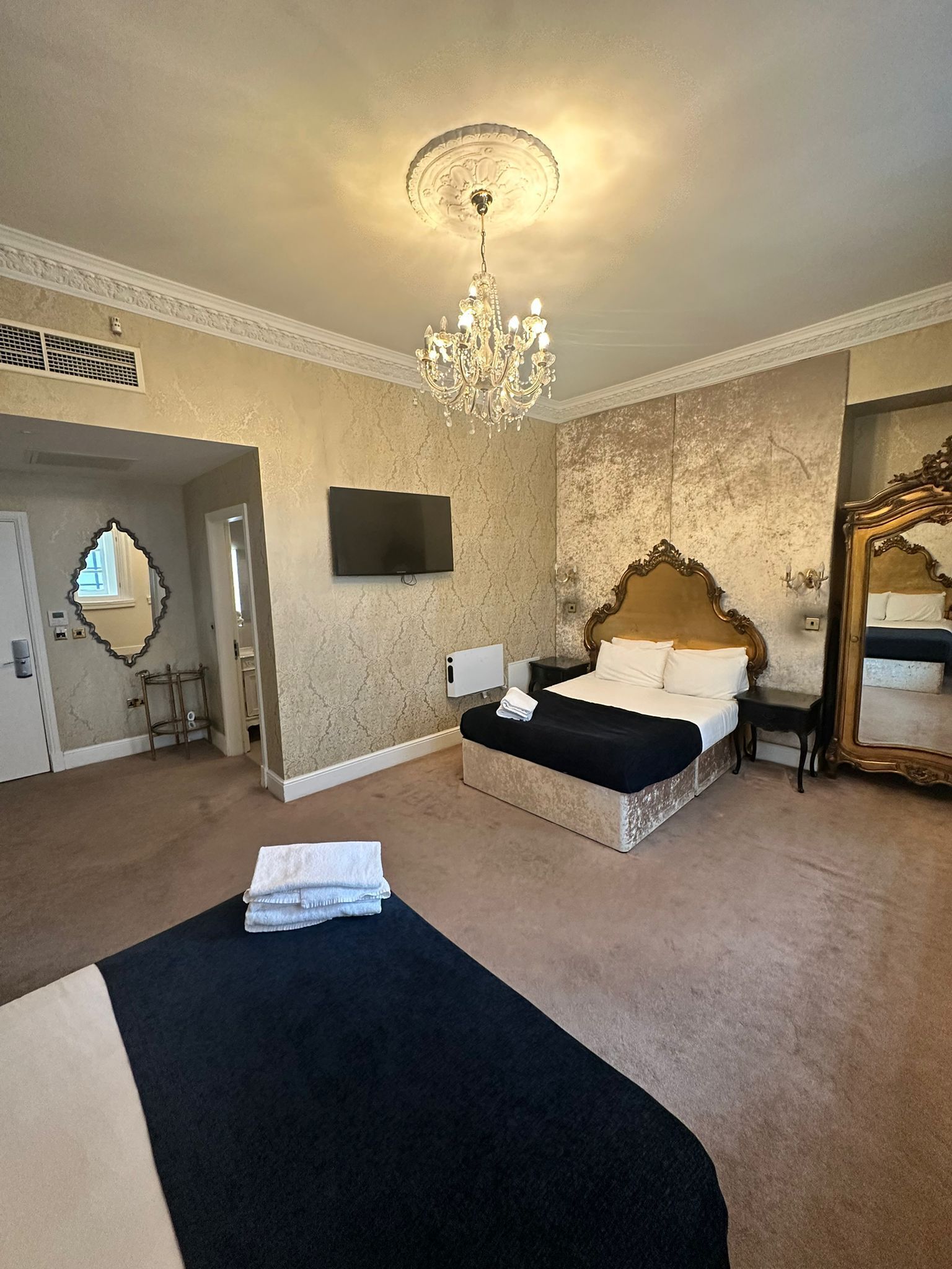 A hotel room with a large bed, a chandelier, a television, and a mirror.