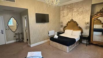 A hotel room with a large bed, a chandelier, a television, and a mirror.