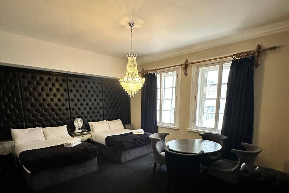 Una habitación de hotel moderna con un sofá tapizado negro, una mesa de comedor redonda y una araña.