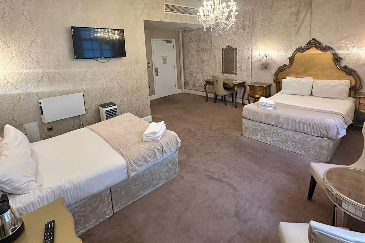 Habitación de hotel con dos camas, televisión, candelabro, escritorio con control remoto y una silla.