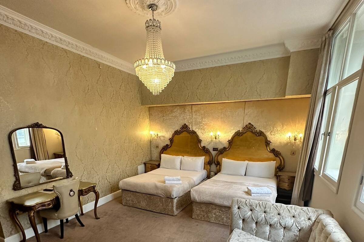 Una habitación de hotel con una cama grande, un sillón de descanso, un tocador con espejo y un candelabro.