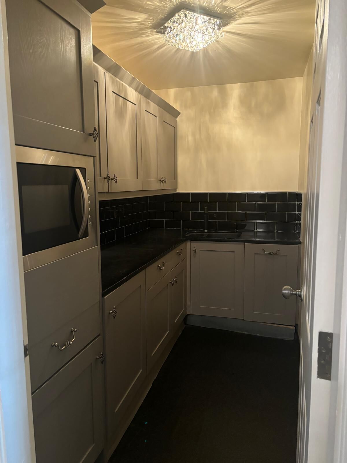 A kitchen with a microwave, cabinets, and a black tiled backsplash.